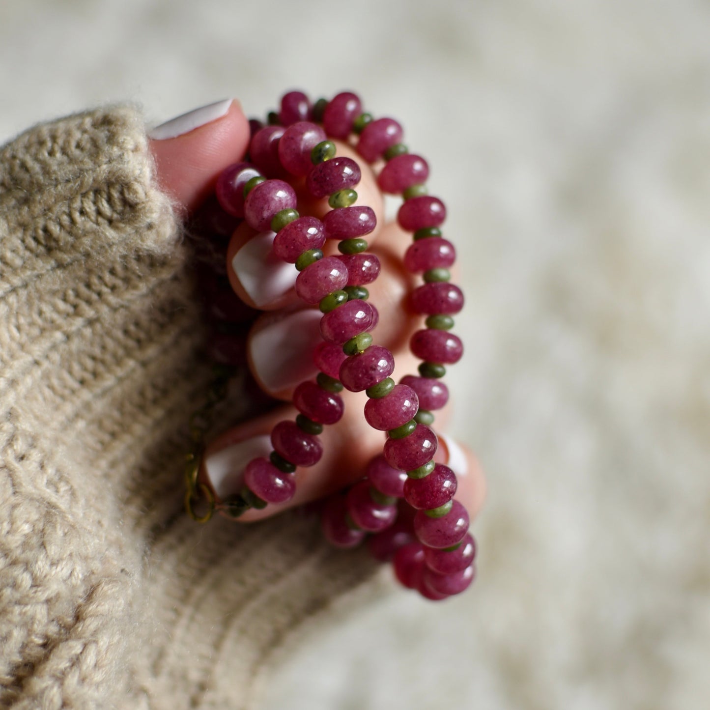 Hand holding a pink beaded necklace against a neutral background