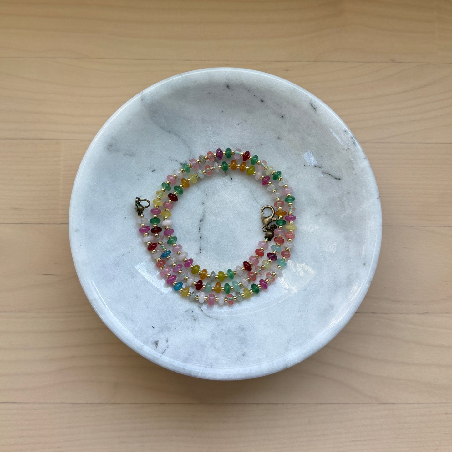 Colorful beaded bracelet in a white marble dish on a wooden surface