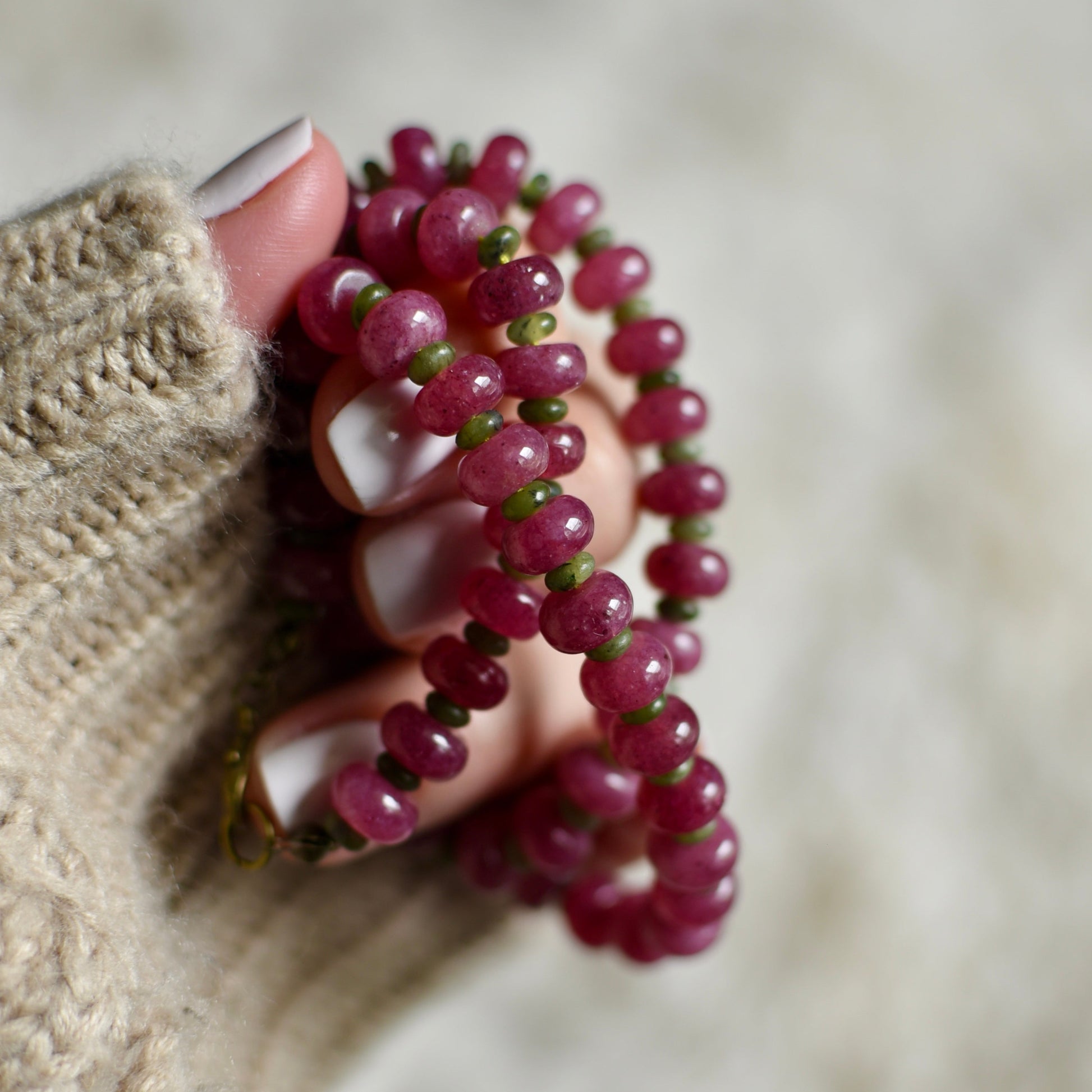 Hand holding a pink beaded necklace against a neutral background
