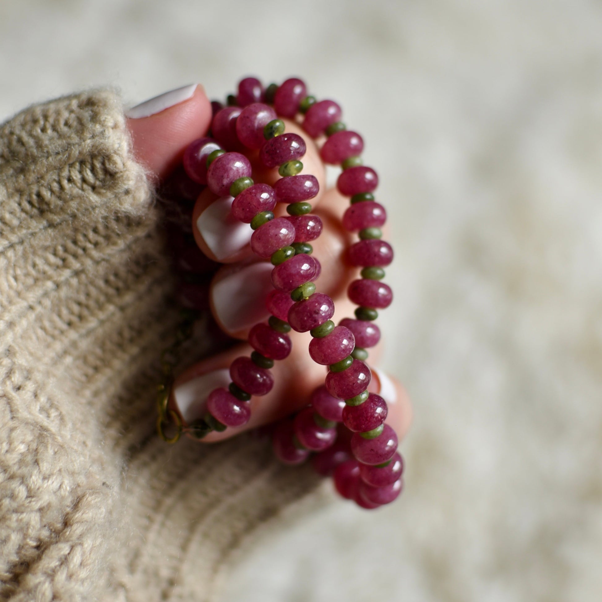 Hand holding a pink beaded necklace against a neutral background
