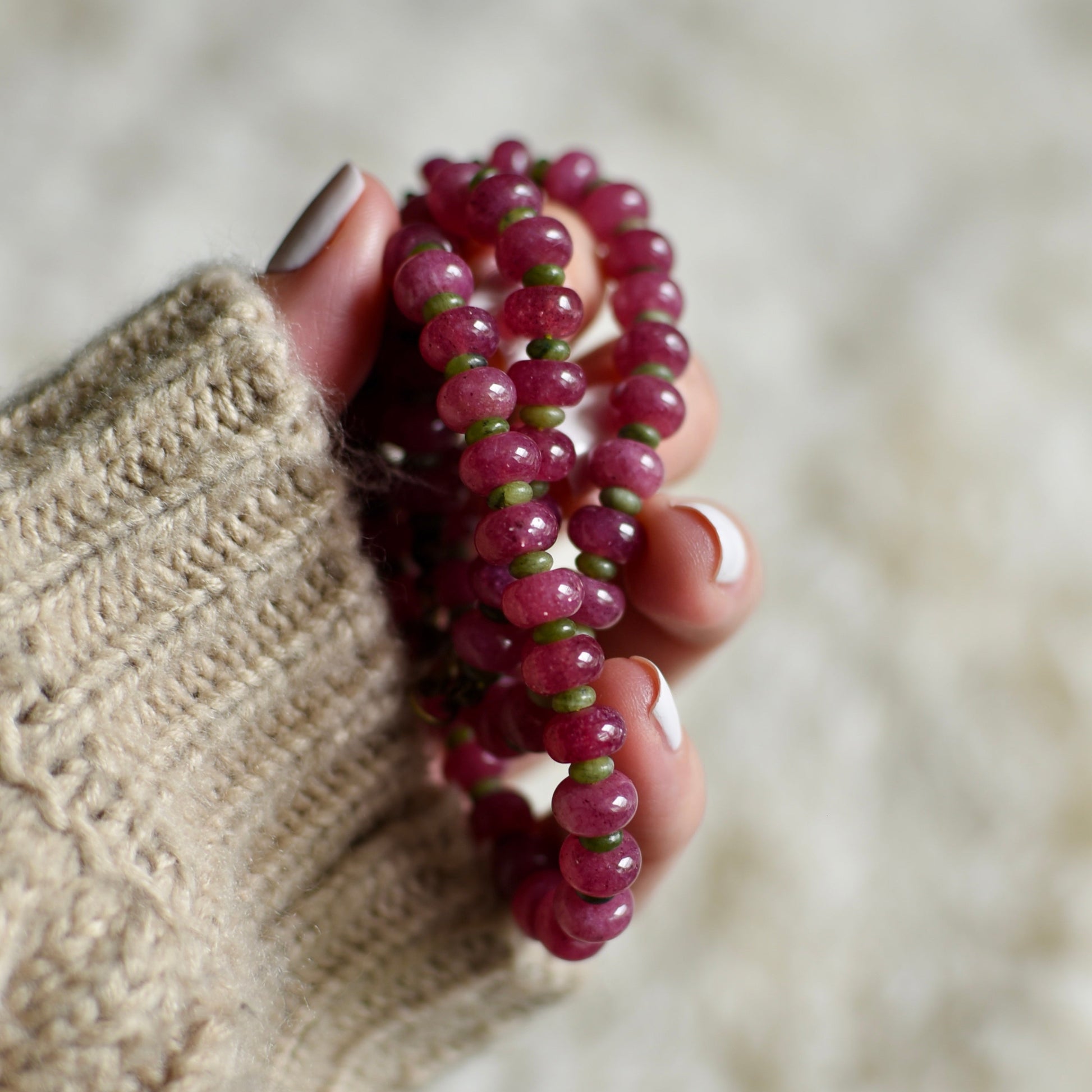 Hand holding a pink beaded bracelet against a neutral background