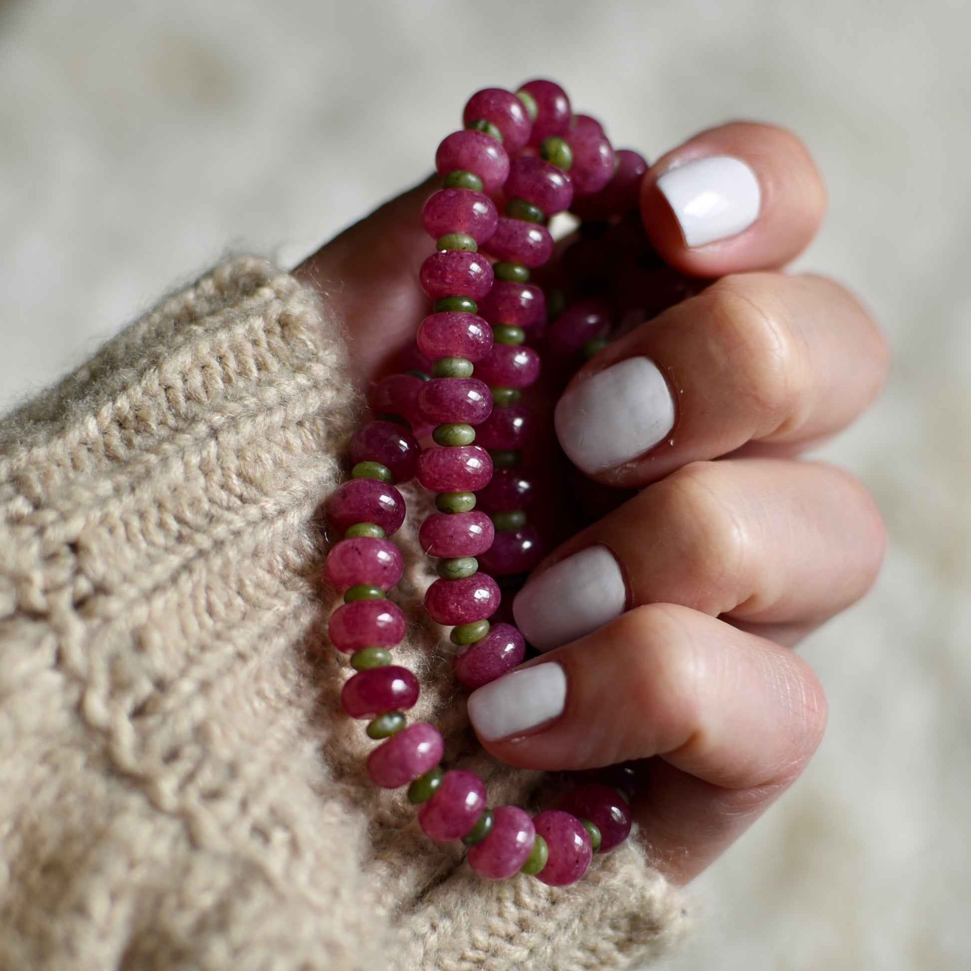Hand holding a pink beaded necklace against a neutral background