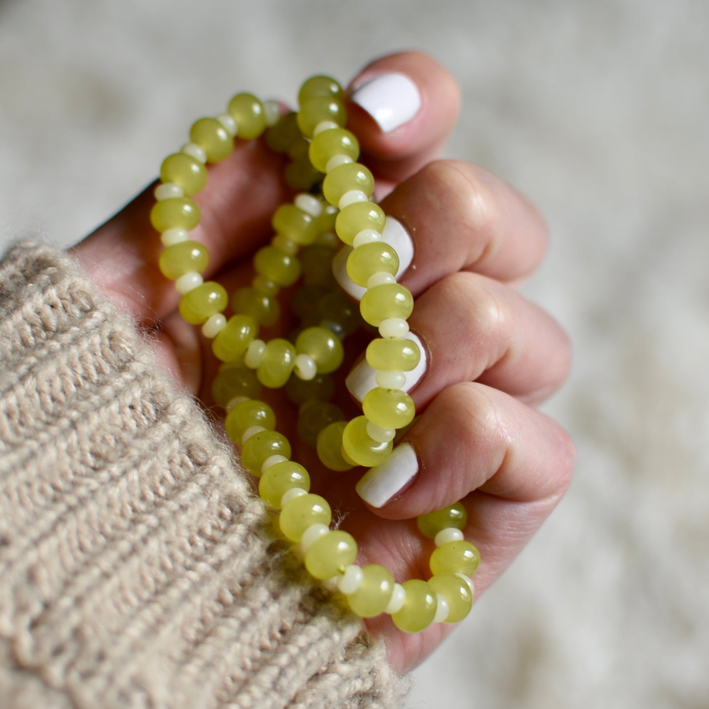Hand holding a green beaded bracelet against a blurred background