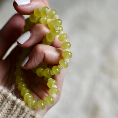 Hand holding a green beaded bracelet against a blurred background