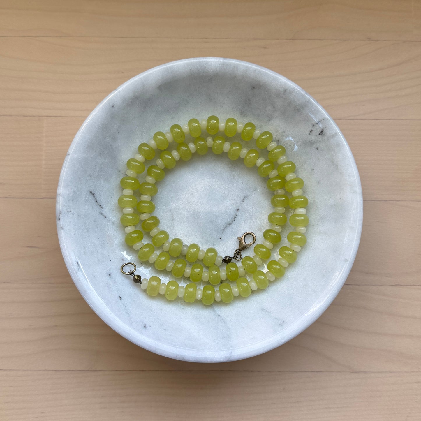 Green beaded necklace in a white marble bowl on a wooden surface