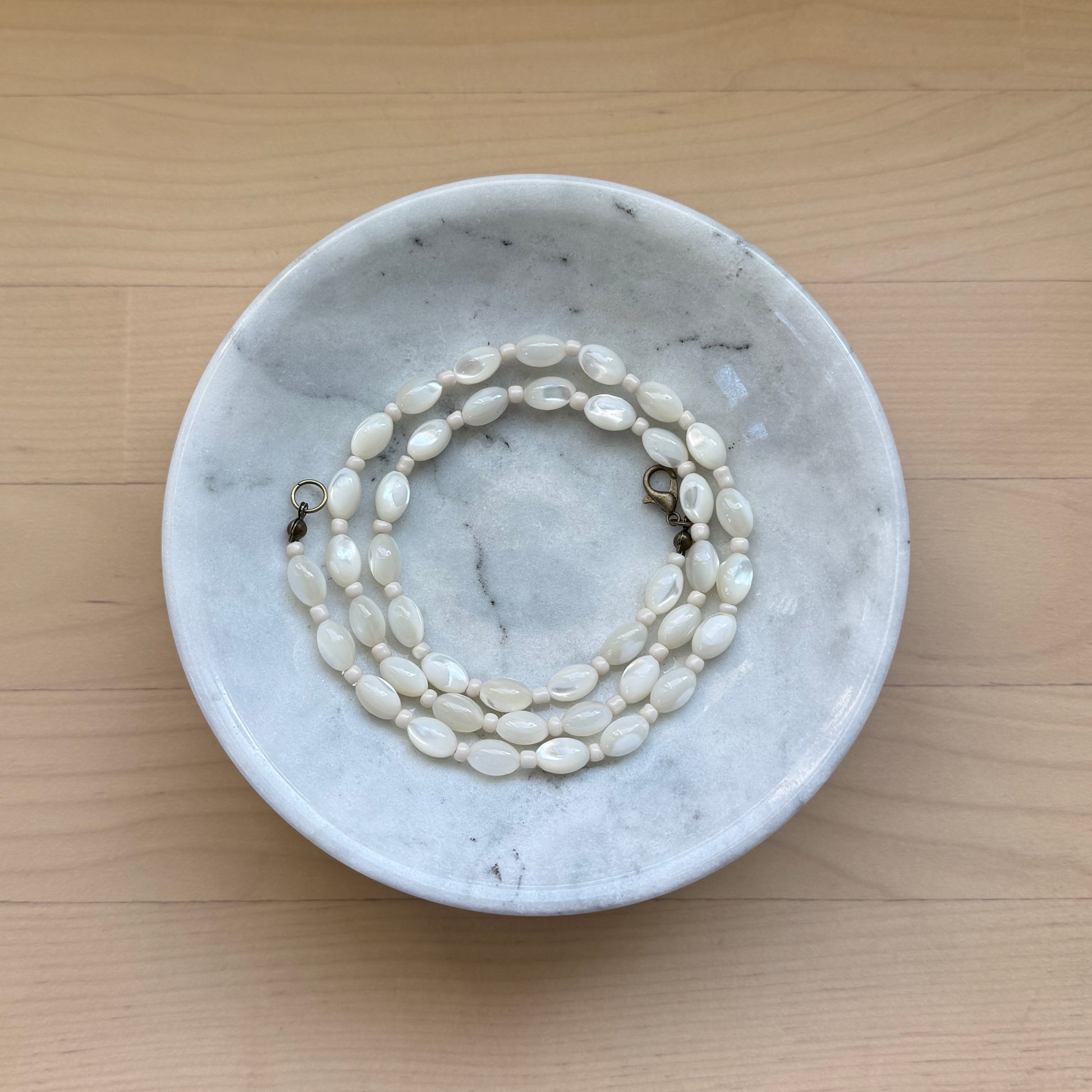 Marble dish with a pearl necklace on a wooden surface
