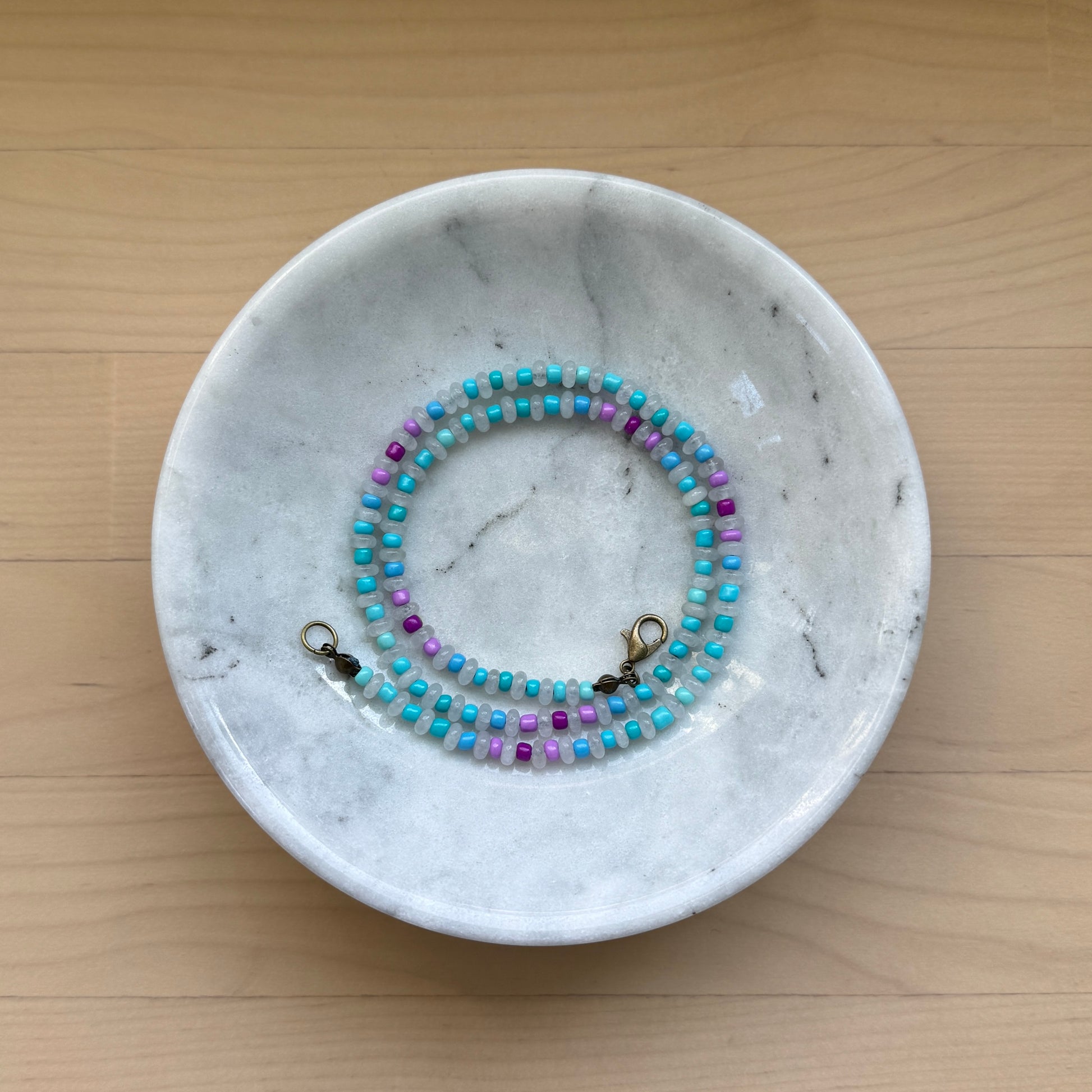 Marble jewelry dish with a beaded necklace on a wooden surface