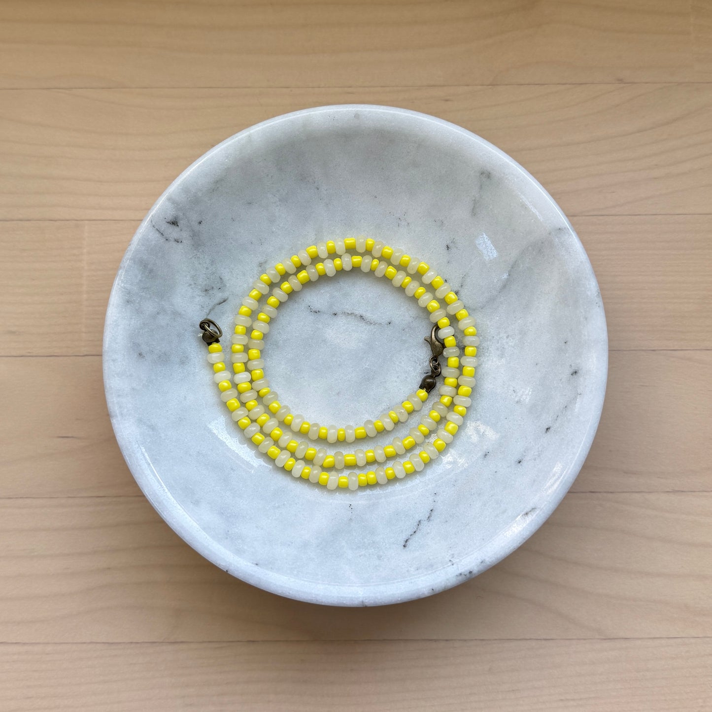 Marble-patterned dish with a yellow beaded bracelet on a wooden surface