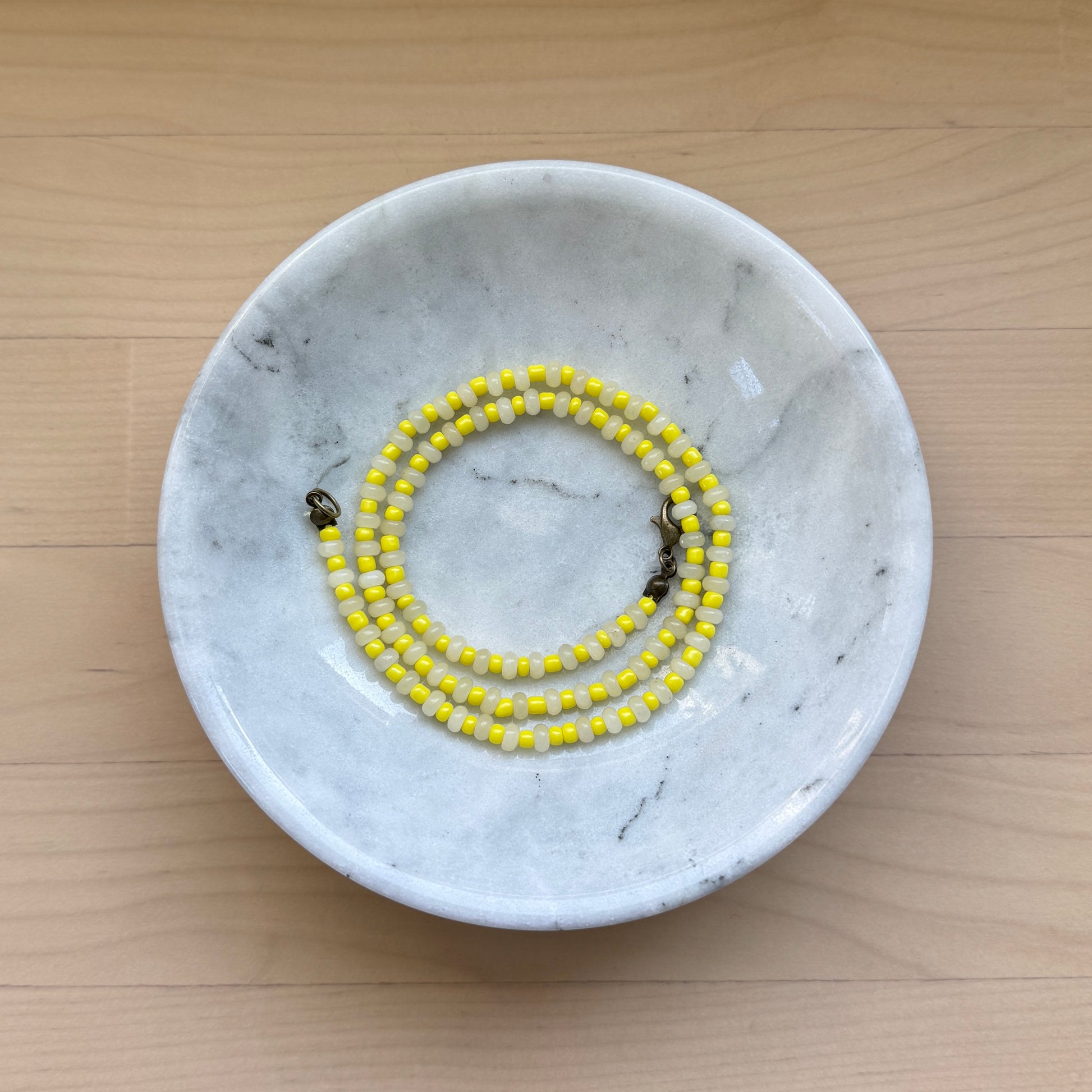 Marble-patterned dish with a yellow beaded bracelet on a wooden surface