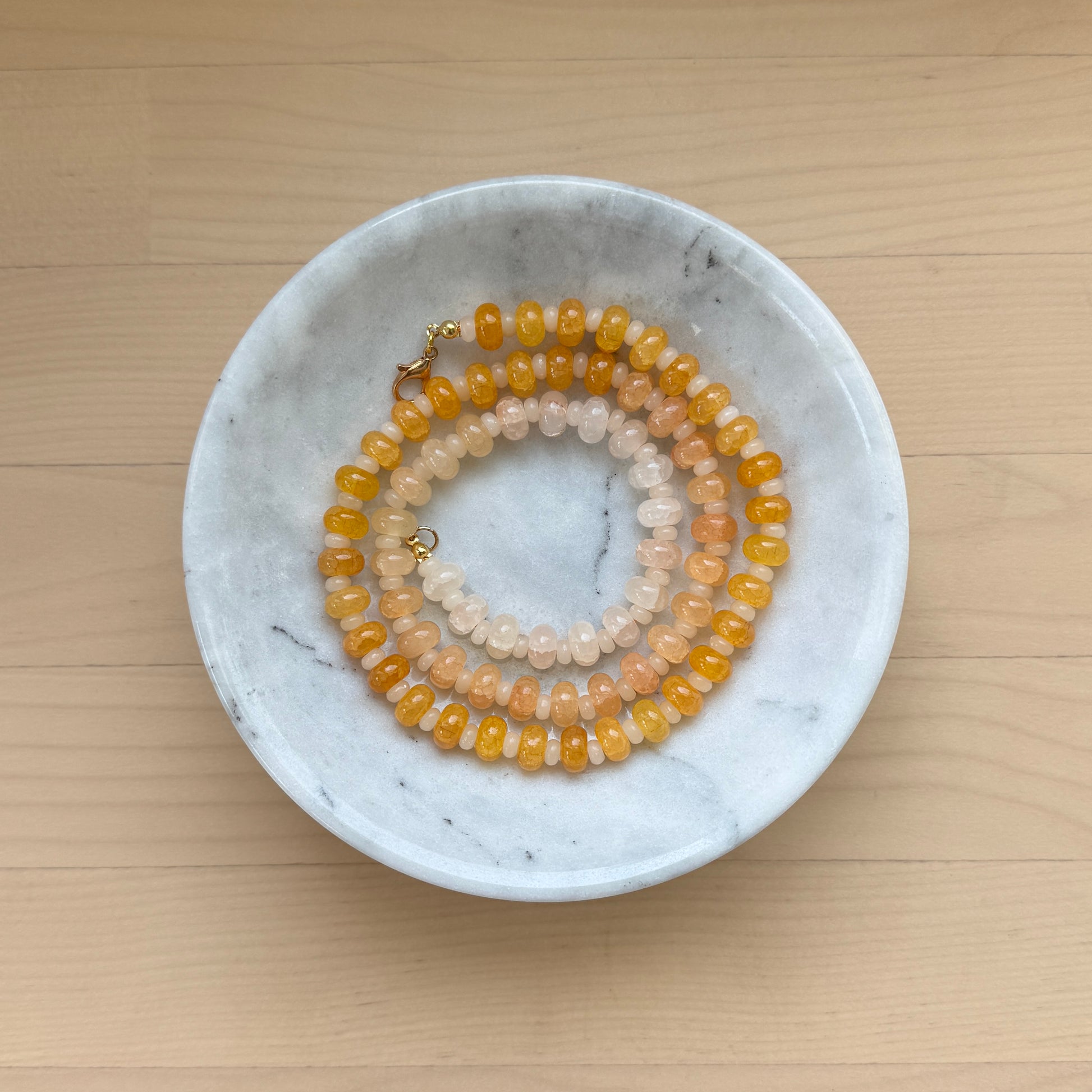 Two beaded necklaces in a marble dish on a wooden surface