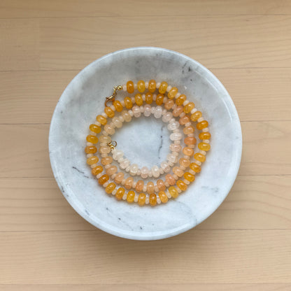 Two beaded necklaces in a marble dish on a wooden surface