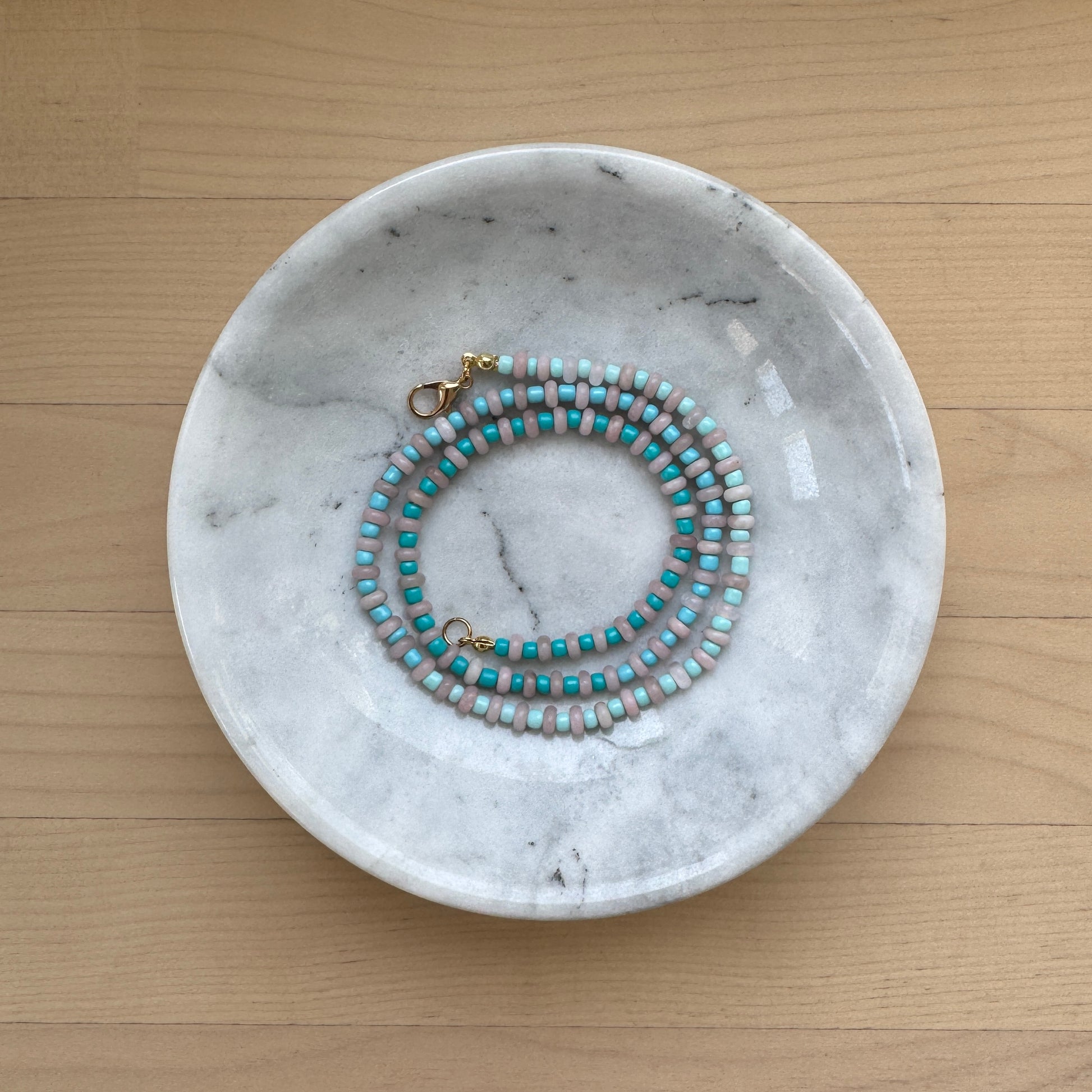 Marble-patterned dish with a beaded necklace on a wooden surface