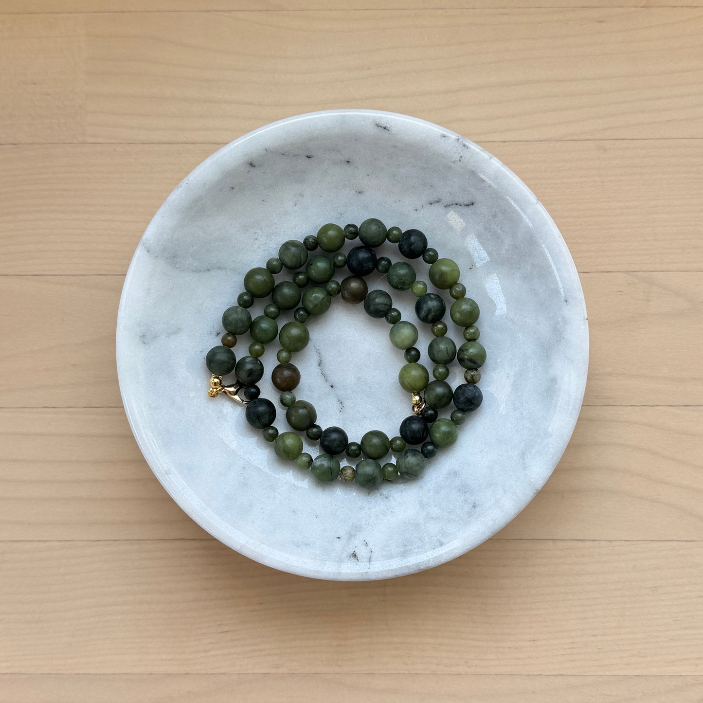 Green beaded necklace in a white marble dish on a wooden surface