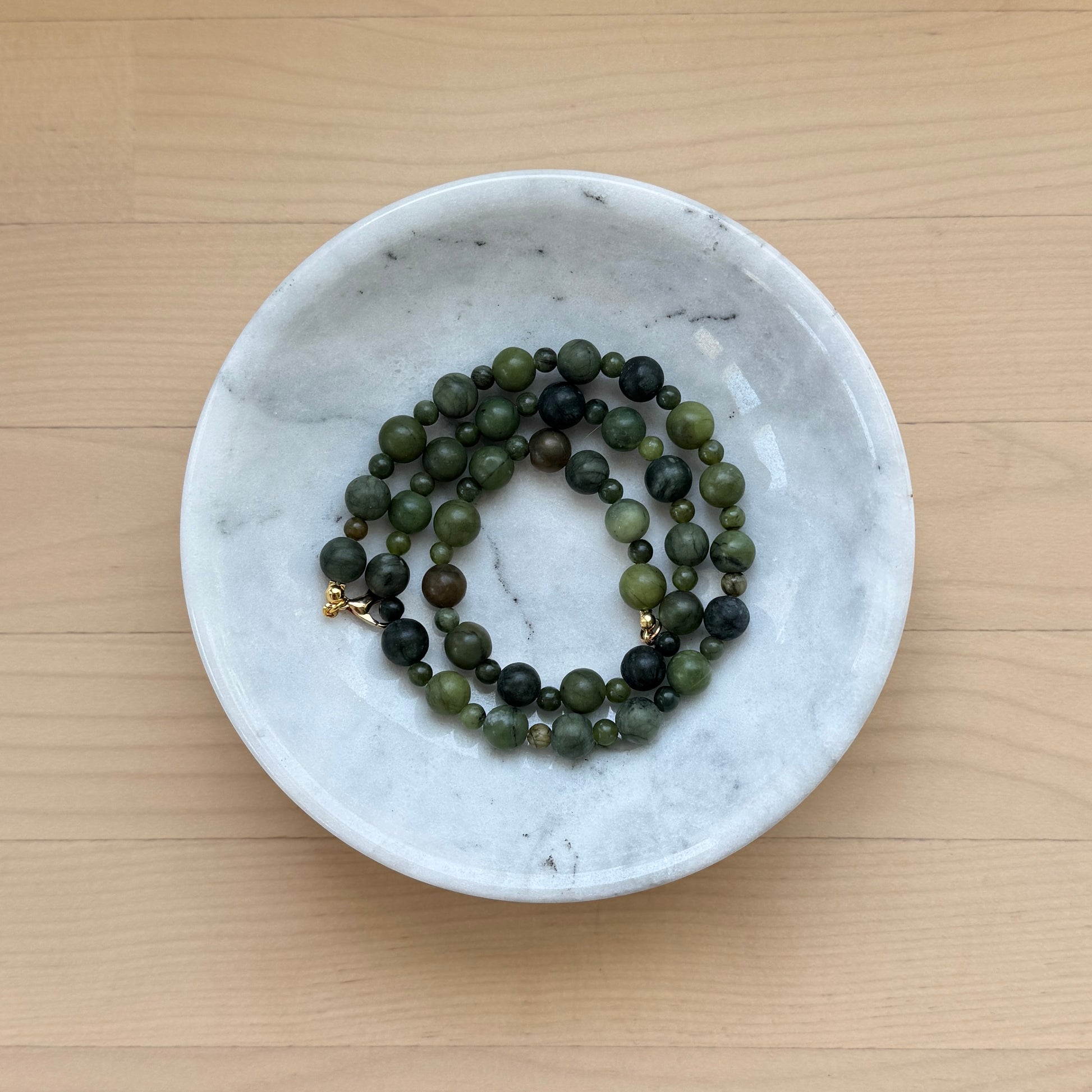 Green beaded necklace in a white marble dish on a wooden surface